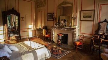 Un dormitorio con cama, chimenea, espejo y escritorio.