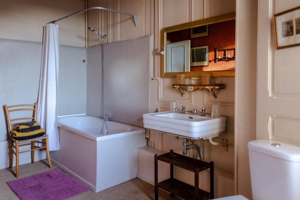 Une salle de bain avec une baignoire, un lavabo, une douche, une chaise et une petite table.