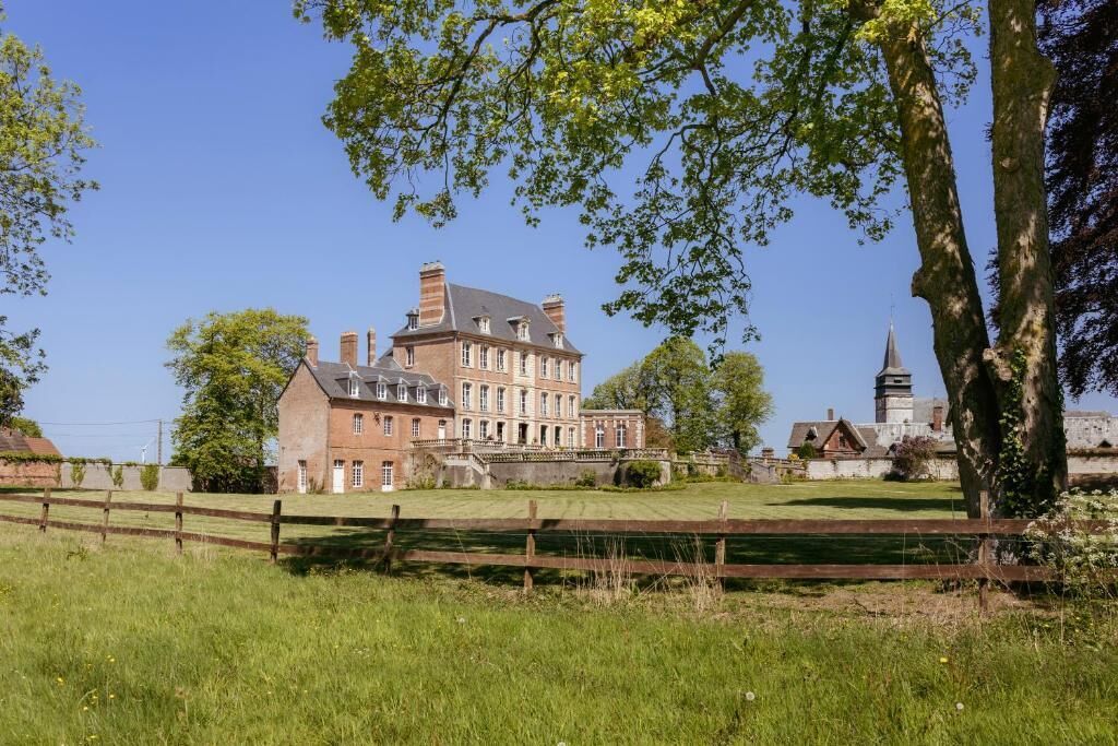 A large, historic building with a prominent central tower, surrounded by a well-maintained lawn and a wooden fence.
