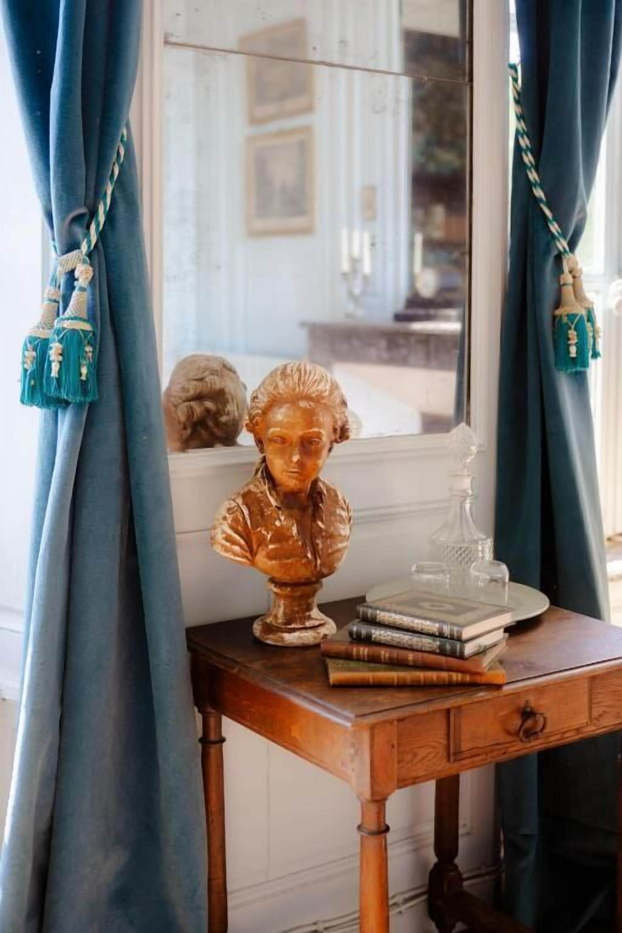 Une table en bois sur laquelle se trouvent un buste sculpté, des livres et un objet en verre.