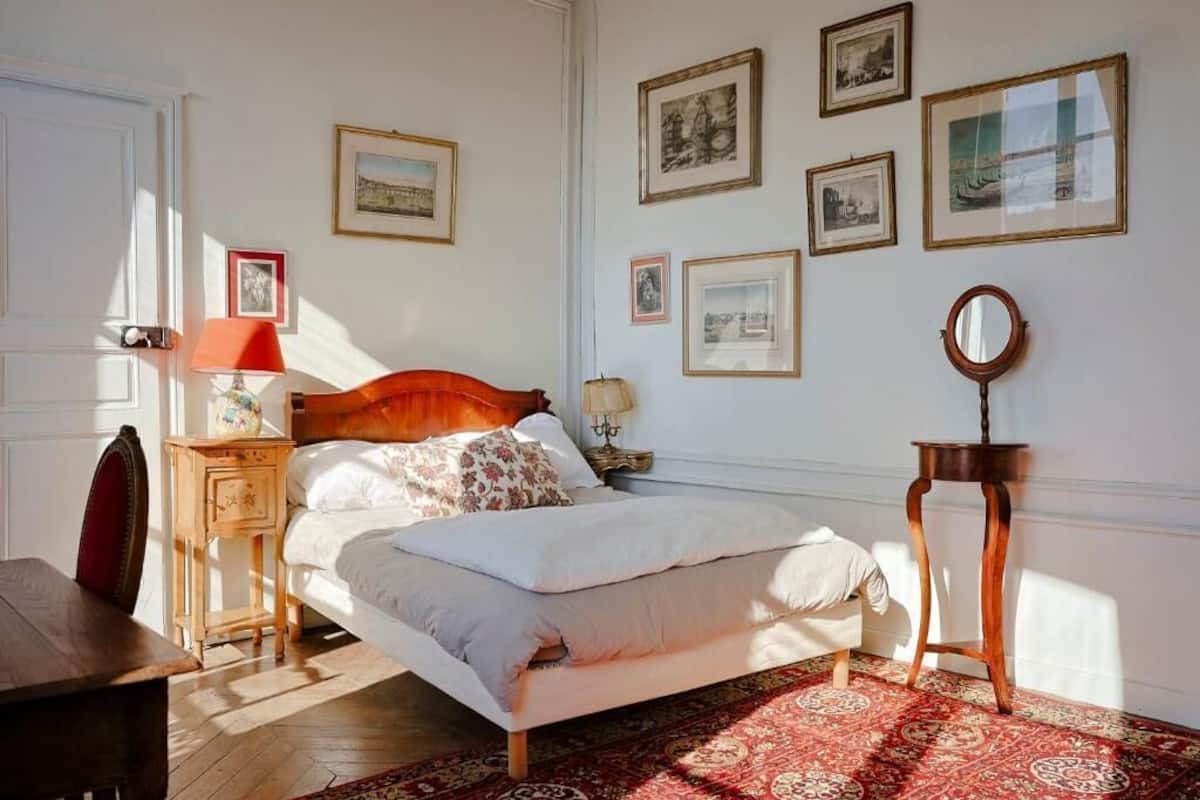 Un dormitorio con cama, mesitas de noche, un espejo y cuadros en la pared.