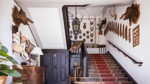 A staircase with patterned carpet, a wooden chair, a cabinet, and wall-mounted animal heads.