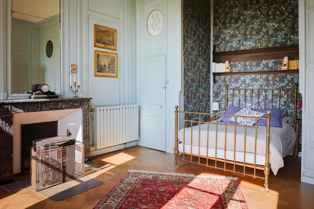 Un dormitorio con cama, chimenea, espejo y pared con diseño.
