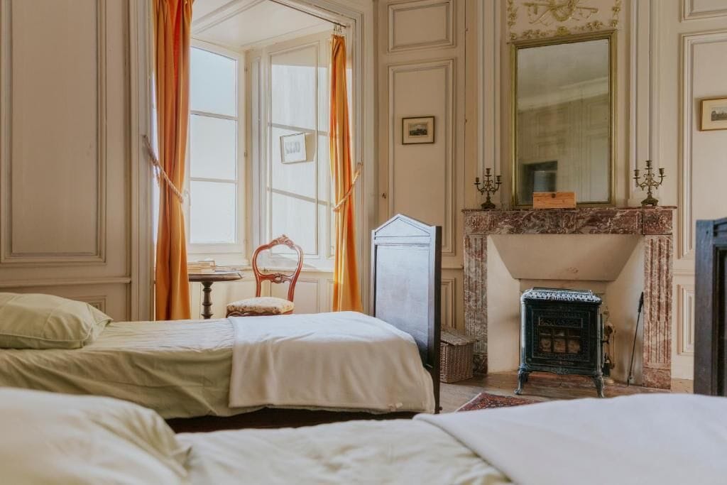 Quarto tradicional com duas camas, lareira e um espelho grande.