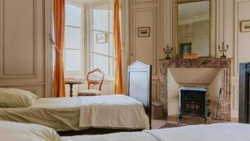 Quarto tradicional com duas camas, lareira e um espelho grande.