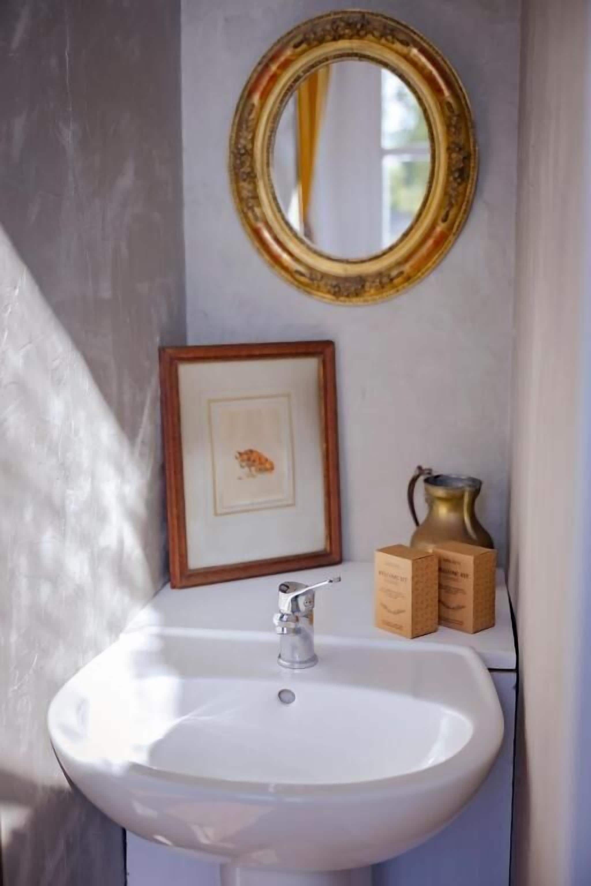 A bathroom with a white sink, a framed picture, a mirror, and a vase.