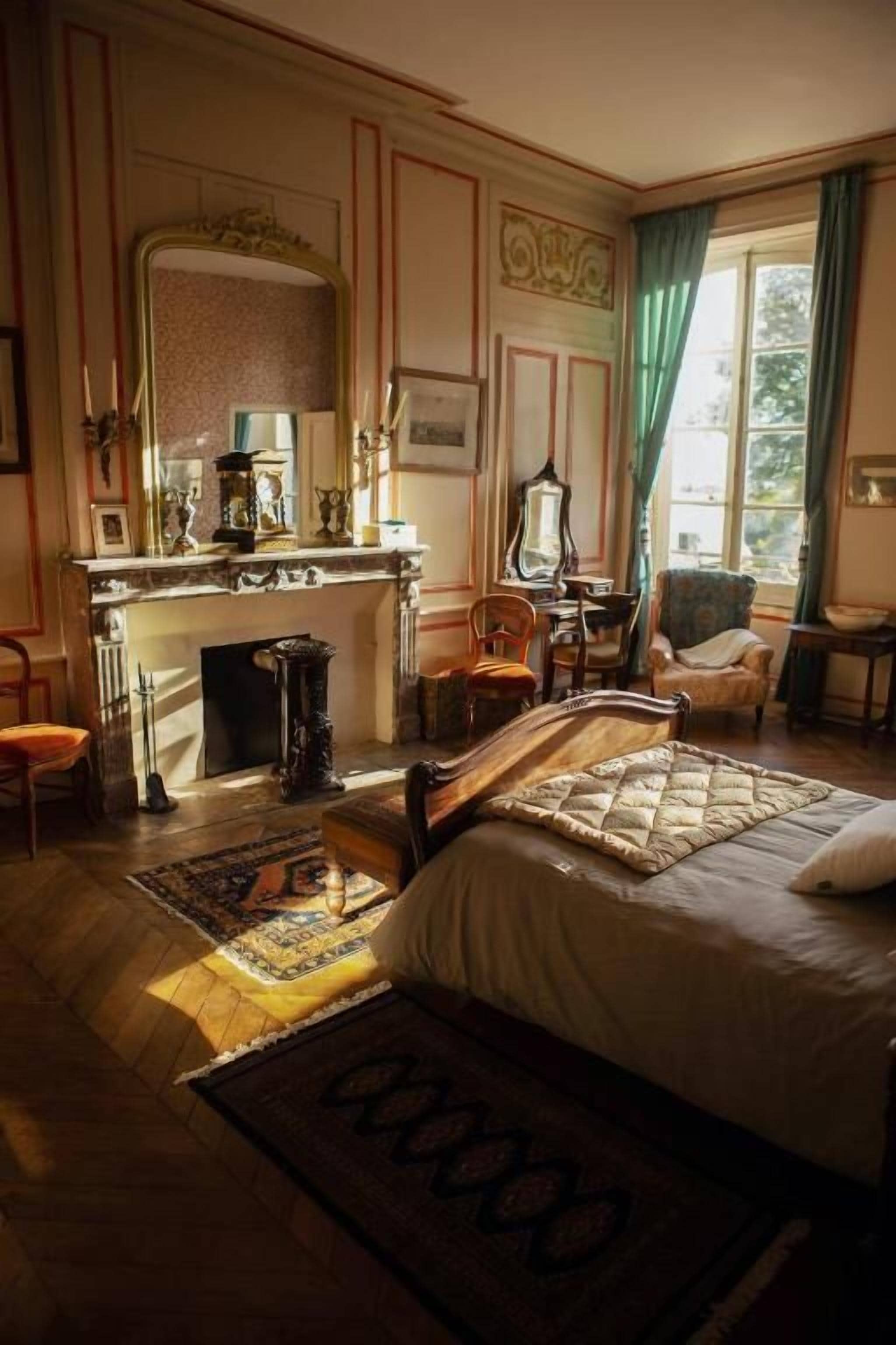 Une chambre à coucher avec un grand lit, une cheminée, un miroir et une fenêtre avec des rideaux.
