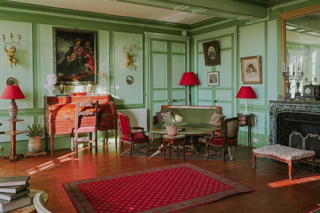 A room with green walls, a fireplace, a red rug, and a dining table with chairs.