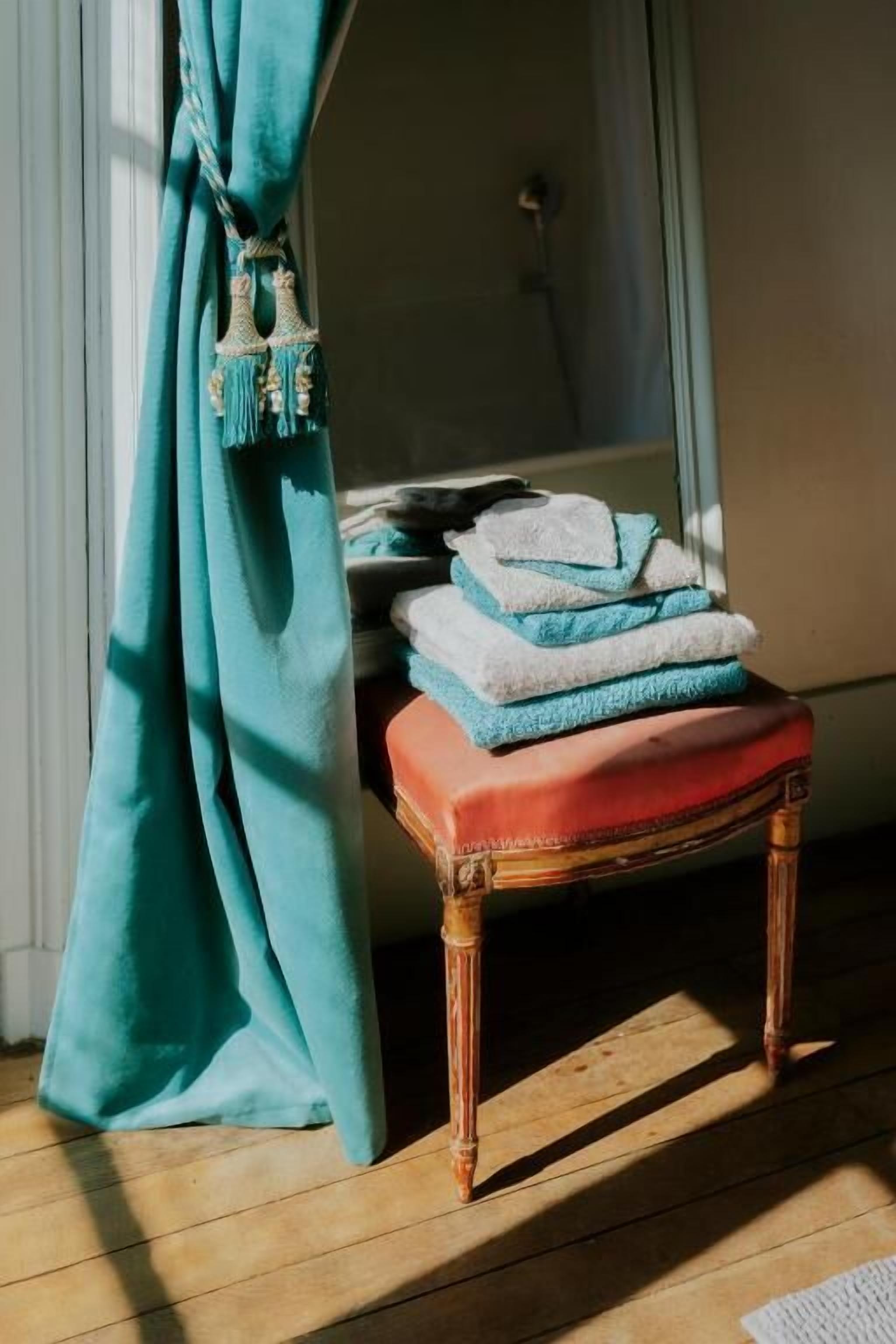 A wooden bench with a stack of folded towels, a teal curtain, and a window with sunlight.