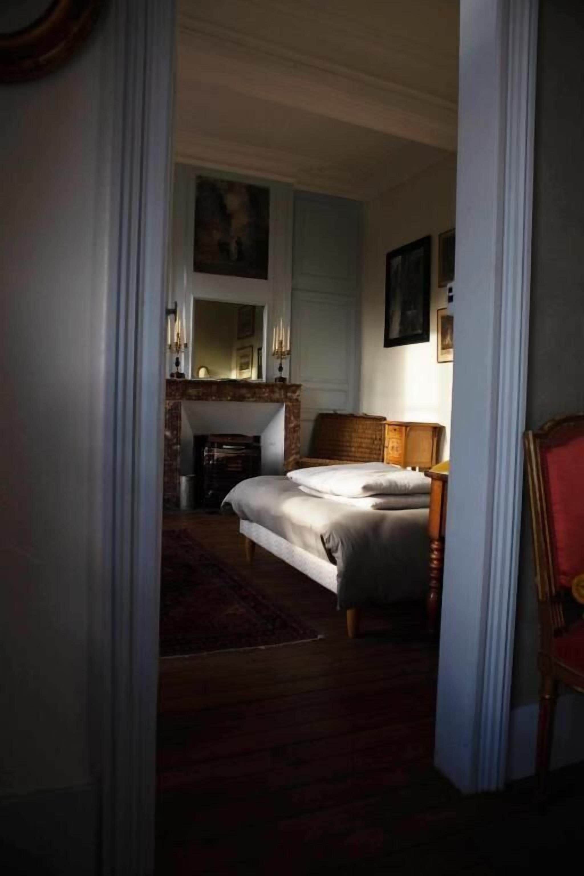 Une chambre à coucher avec un lit, une table de chevet, un miroir, une cheminée et un tableau au mur.