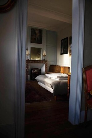 A bedroom with a bed, a nightstand, a mirror, a fireplace, and a painting on the wall.