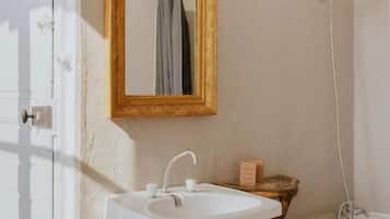 Een badkamer met een wit wastafelmeubel, een spiegel met gouden lijst, een bad en een handdoek aan de muur.