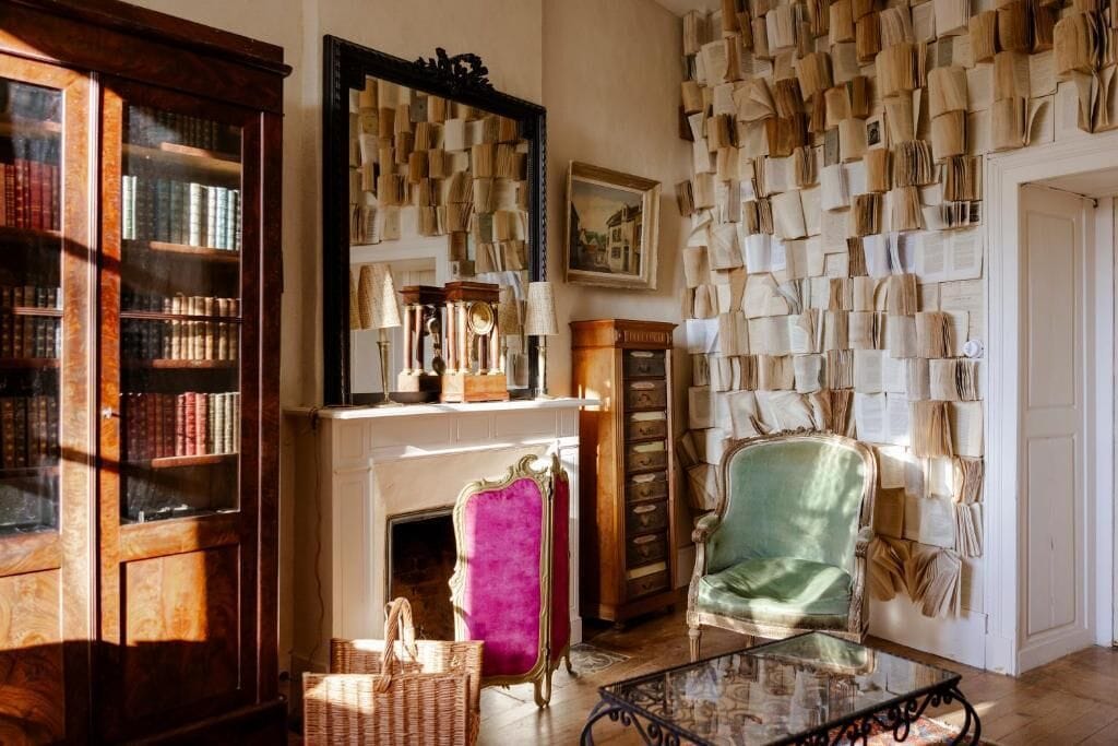 A room with a fireplace, a bookshelf, a mirror, and a wall covered with books.