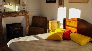 Un dormitorio con cama, chimenea, espejo y cuadros en la pared.
