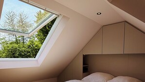 A bedroom with a skylight, wooden flooring, and built-in headboard.