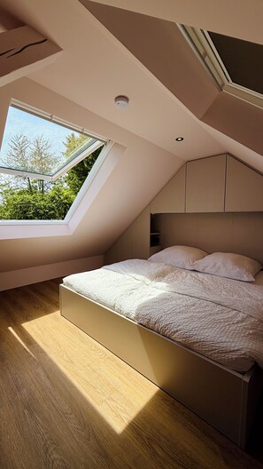 A bedroom with a skylight, wooden flooring, and built-in headboard.