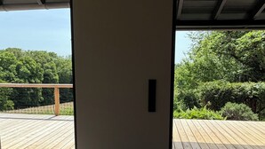 An interior space with a wooden deck, a door leading outside, and a view of greenery.