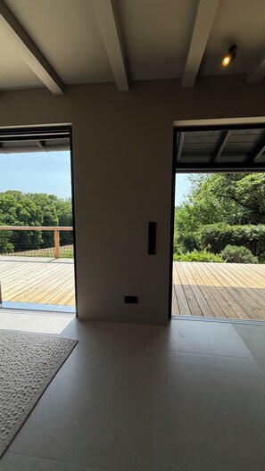 An interior space with a wooden deck, a door leading outside, and a view of greenery.