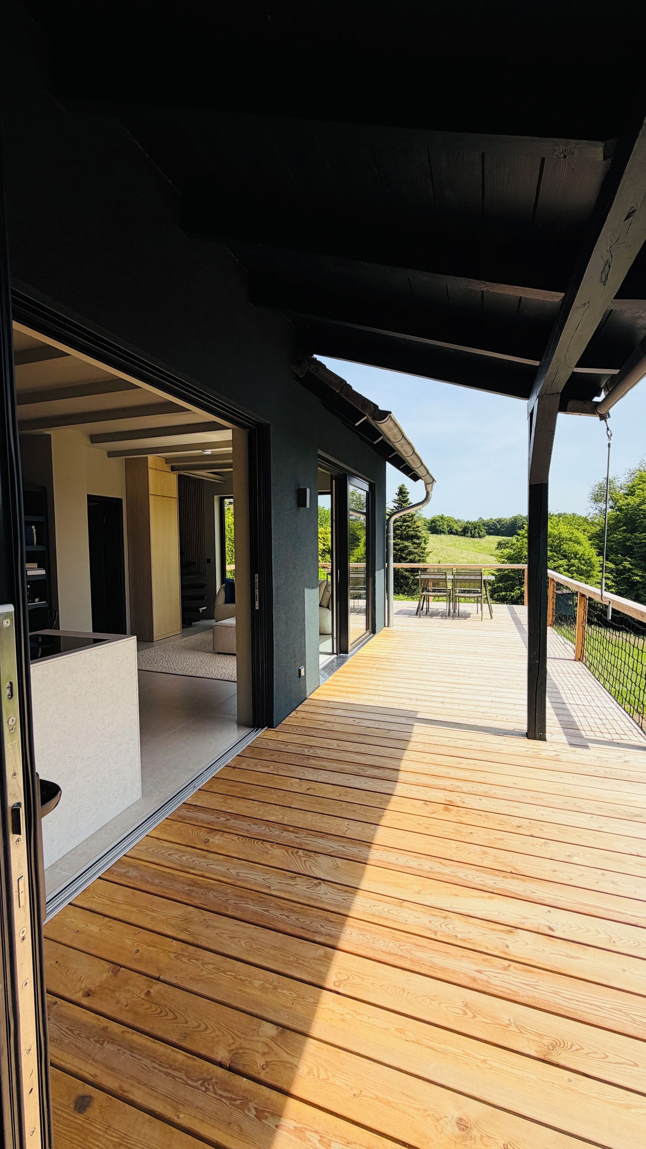 An open wooden deck leading to a covered outdoor area with a view of a green landscape.
