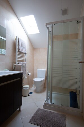 Un baño con tragaluz, inodoro, ducha con puertas de vidrio y tocador de color oscuro.