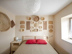 Un dormitorio con cama, mesita de noche, lámpara y un muro decorado con cestas tejidas.