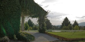 A paved pathway leading to a covered area with a stone archway, surrounded by greenery and a park with a pond. - Apartment 'Saqa Organic Farm' with Mountain View, Wi-Fi and Air Conditioning (Teixoso)