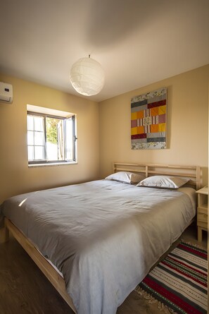 Una camera da letto con un letto, una finestra, un condizionatore d'aria a parete e una coperta colorata.