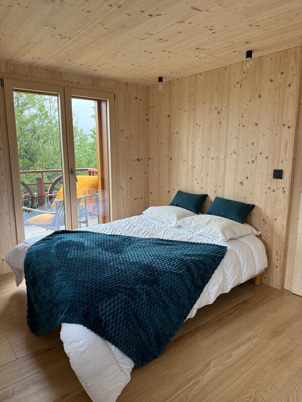 A wooden-paneled room with a bed, a window, and a view of greenery outside.
