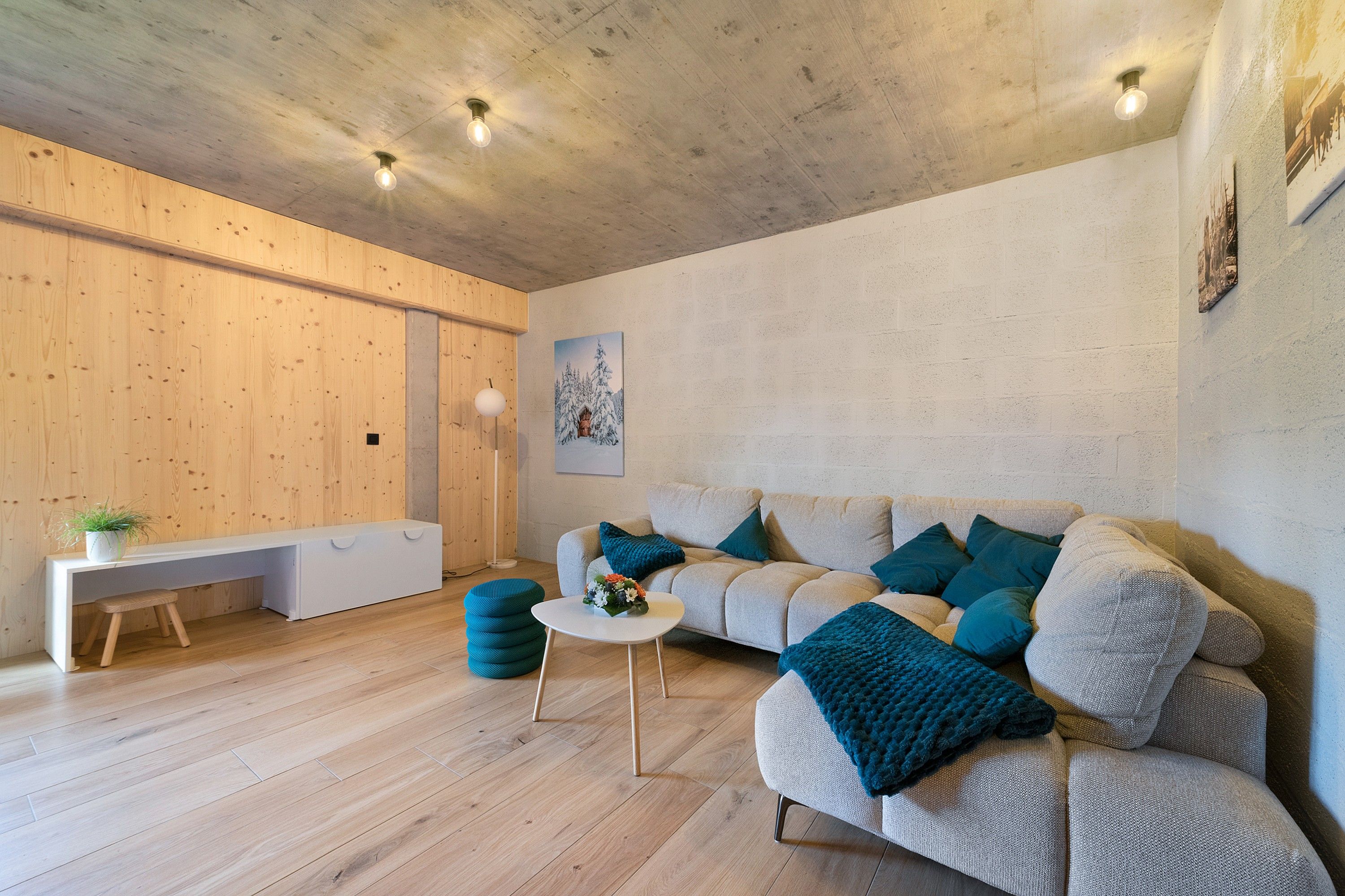 Un salon moderne avec un plancher en bois, un canapé avec des coussins bleus, une table basse blanche et un banc.