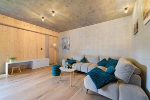Una sala moderna con piso de madera, un sofá con cojines azules, una mesa de centro blanca y un banco.