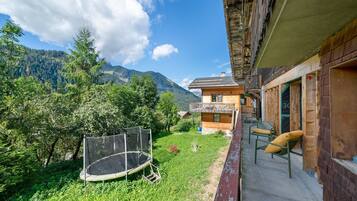 Un chalet en bois doté d’un balcon donnant sur une cour verdoyante et avec une chaîne de montagnes en arrière-plan.