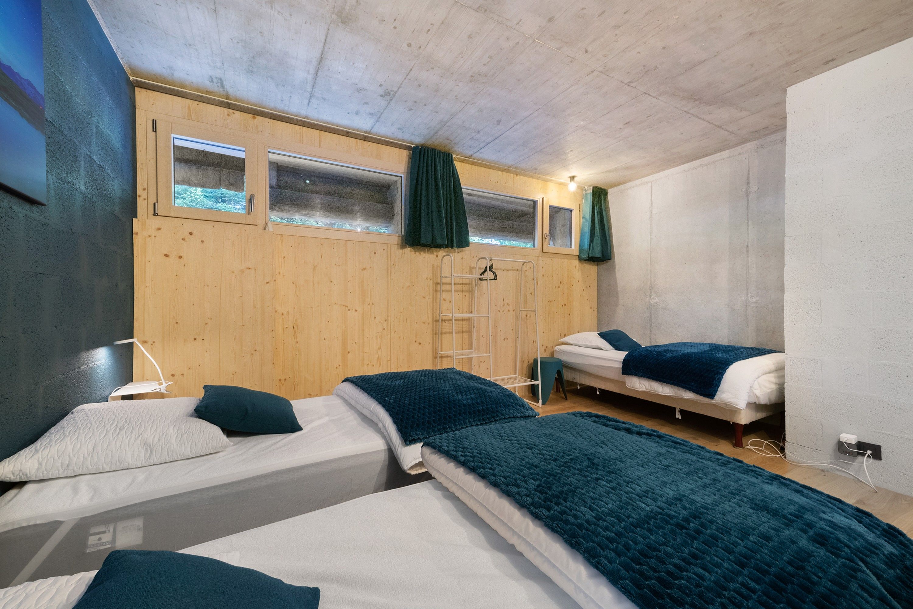 Une pièce avec deux lits, des murs en bois, une fenêtre avec des rideaux, une échelle et une prise de courant.