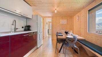 A compact kitchen with modern appliances, a dining area with a wooden table and chairs, and a view through a window.