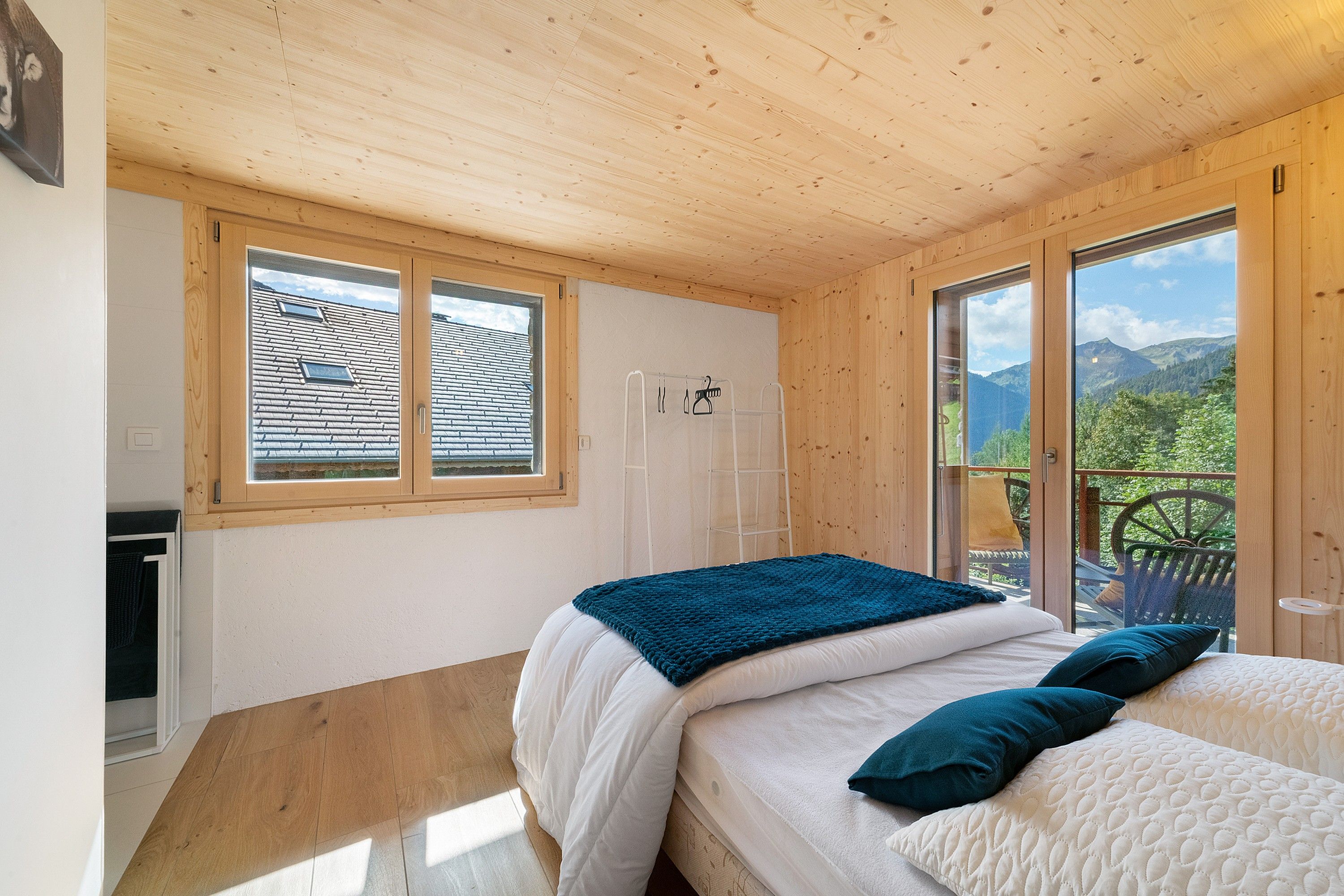 A bedroom with a bed, a window with a view of mountains, and a balcony with a chair.
