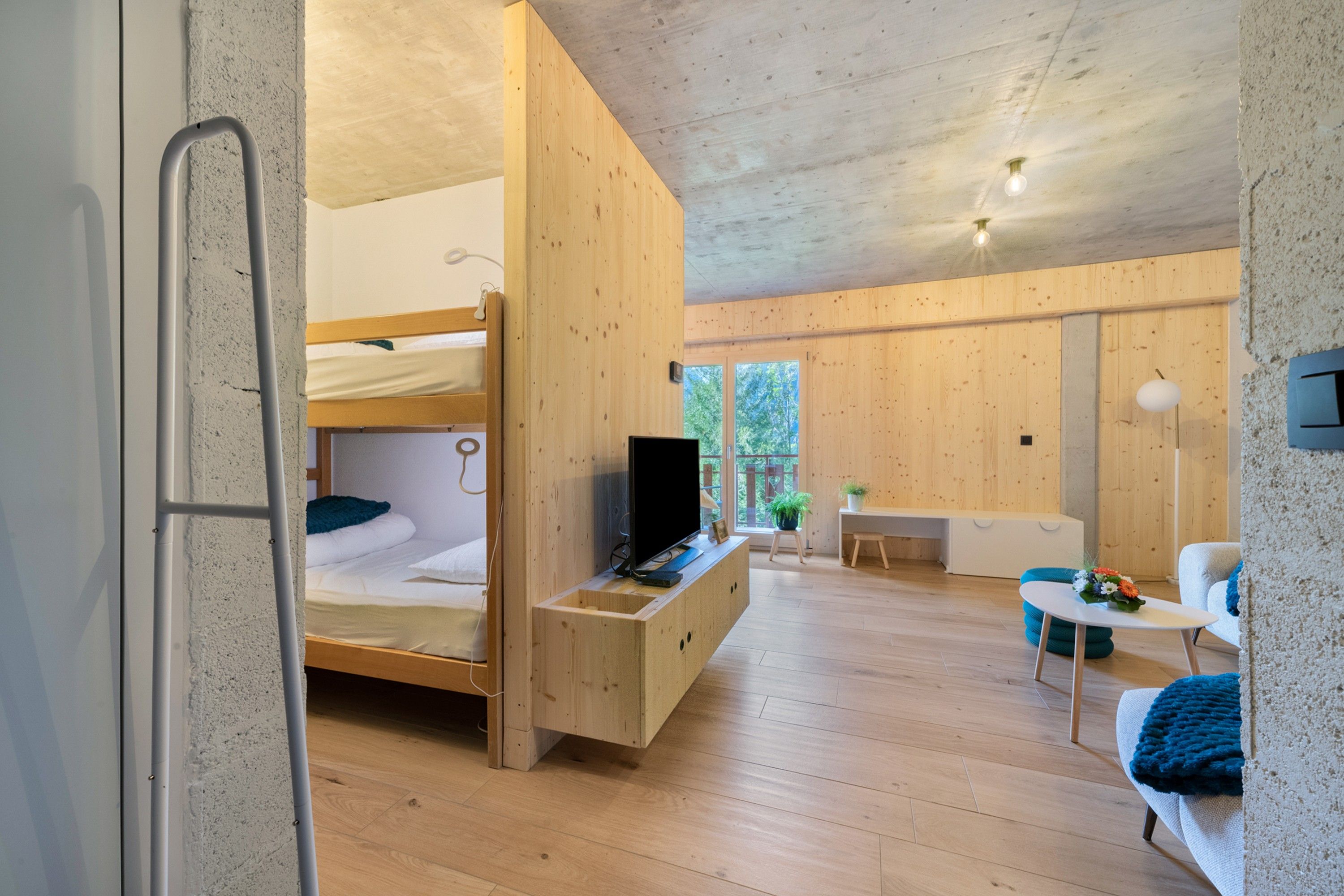 A compact room with a bunk bed, a desk, a chair, and a small table.
