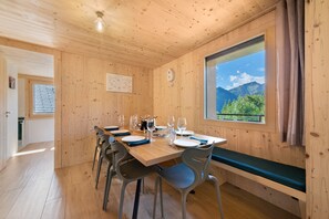 A wooden dining area with a table set for four, chairs, a bench, and a window with a mountain view. - Apartment 'C’Emile - 74390' with Mountain View, Shared Garden, and Wi-Fi (Châtel)