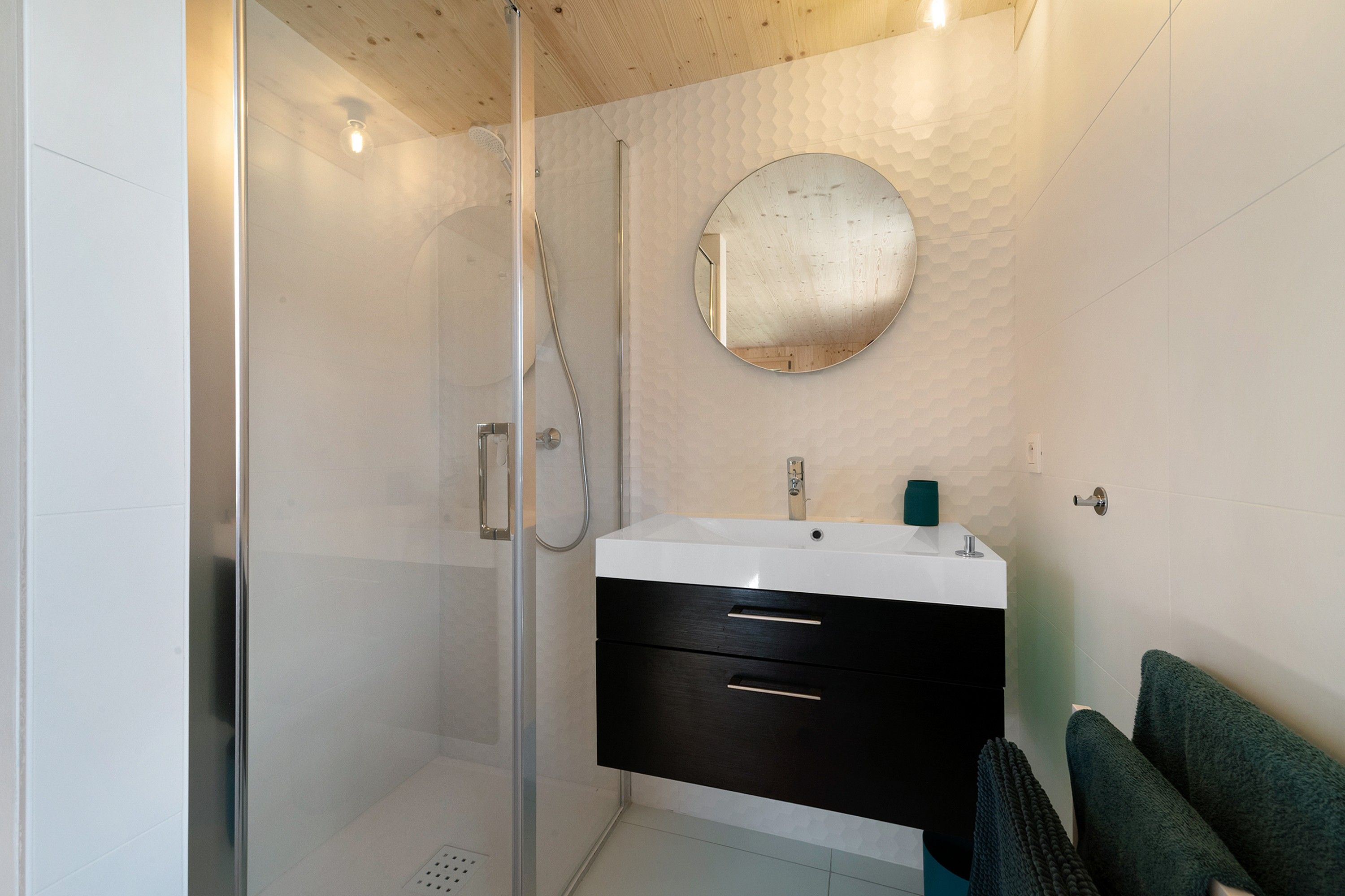 A modern bathroom with a glass-enclosed shower, a round mirror, and a white sink with a black cabinet.