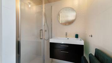 A modern bathroom with a glass-enclosed shower, a round mirror, and a white sink with a black cabinet.