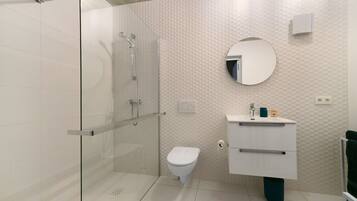 Une salle de bain moderne avec une douche à parois de verre, des toilettes blanches et un meuble-lavabo avec un miroir.