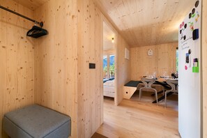 A wooden interior with a bench, a bed, a dining area with chairs, and a refrigerator with magnets. - Apartment 'C’Emile - 74390' with Mountain View, Shared Garden, and Wi-Fi (Châtel)