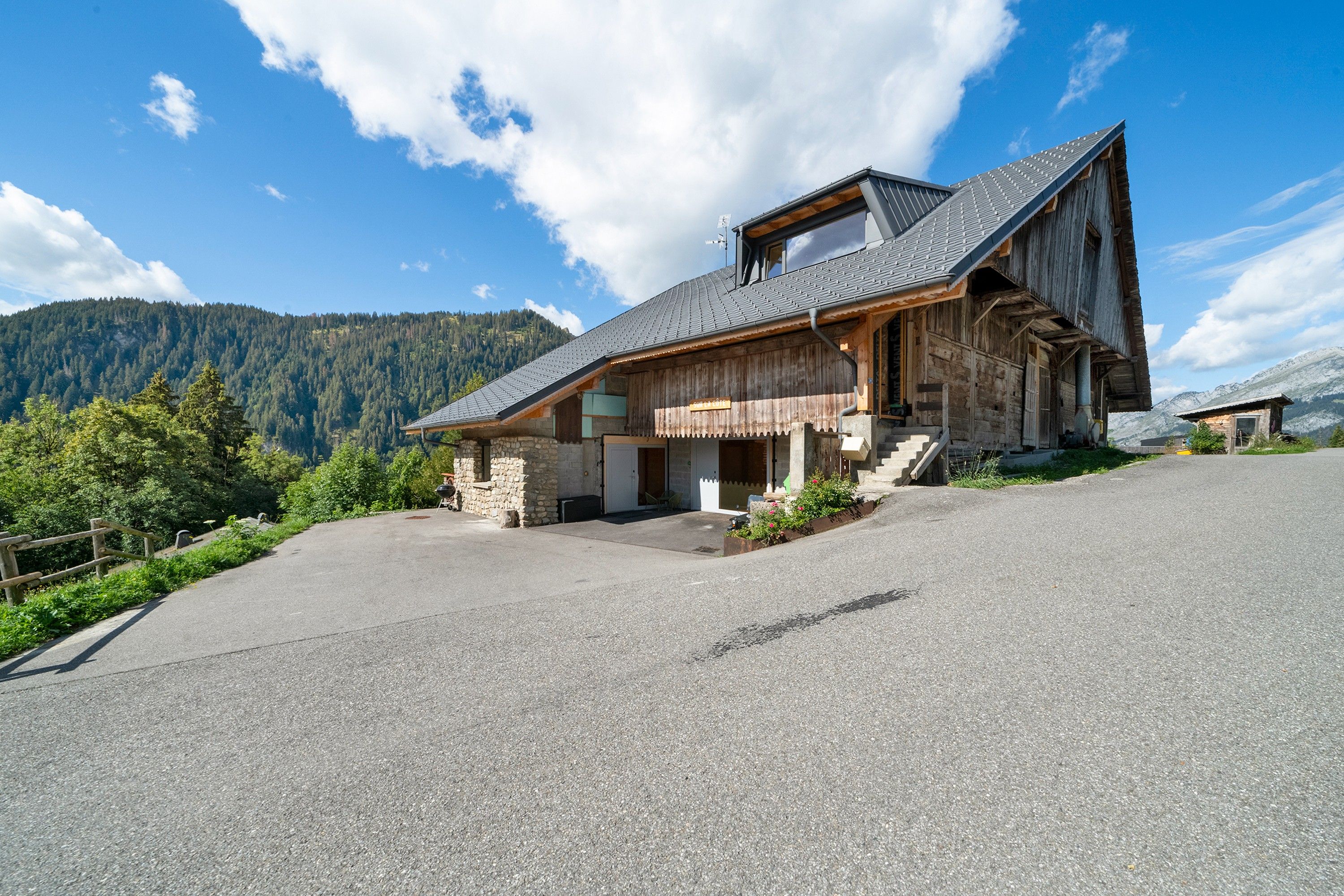 A wooden mountain cabin with a sloped roof, stone foundation, and a paved driveway.