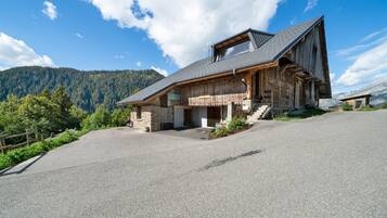A wooden mountain cabin with a sloped roof, stone foundation, and a paved driveway.