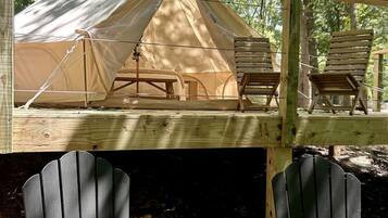 A tent with two chairs on a wooden deck, surrounded by trees.