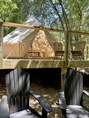 A tent with two chairs on a wooden deck, surrounded by trees.