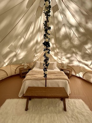 A tented accommodation with a bed, wooden nightstands, and a white fluffy rug.