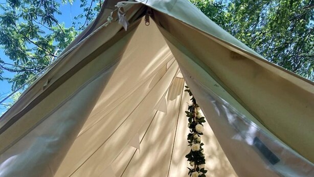 Una tenda con un letto, un tavolino e un frigorifero.