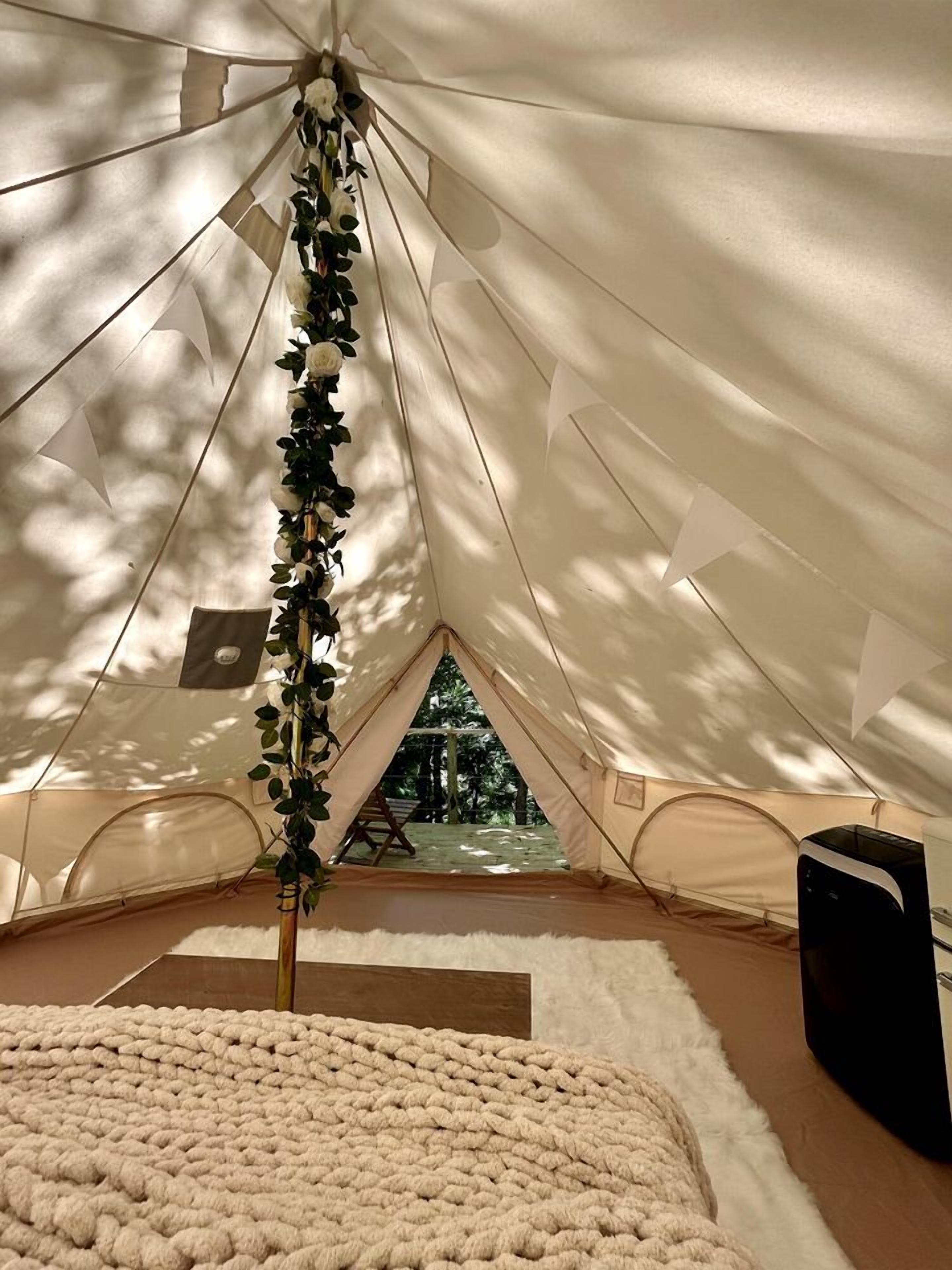 A tent with a view of trees, a white knitted rug, and a black object on the floor.