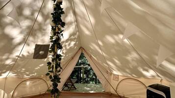 A tent with a view of trees, a white knitted rug, and a black object on the floor.