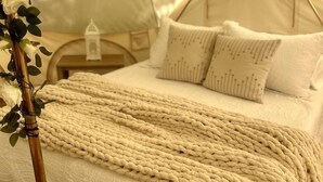 Una tenda con un letto, cuscini, una coperta e un comodino.