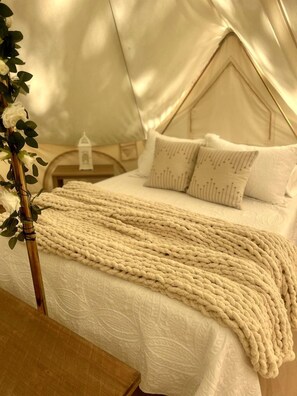 A tented room with a bed, pillows, a blanket, and a bedside table.